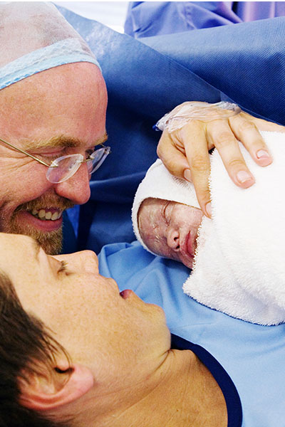 Newborn baby lying on Mum's chest while her and Dad look on smiling