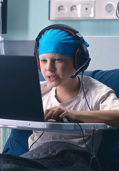 Young boy with cancer playing on his laptop in his hosipital bed