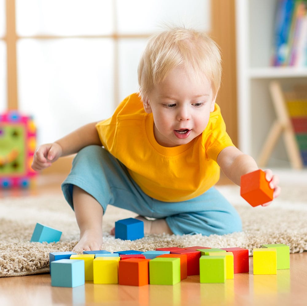 Toddler reaching over to put a red block in a slot