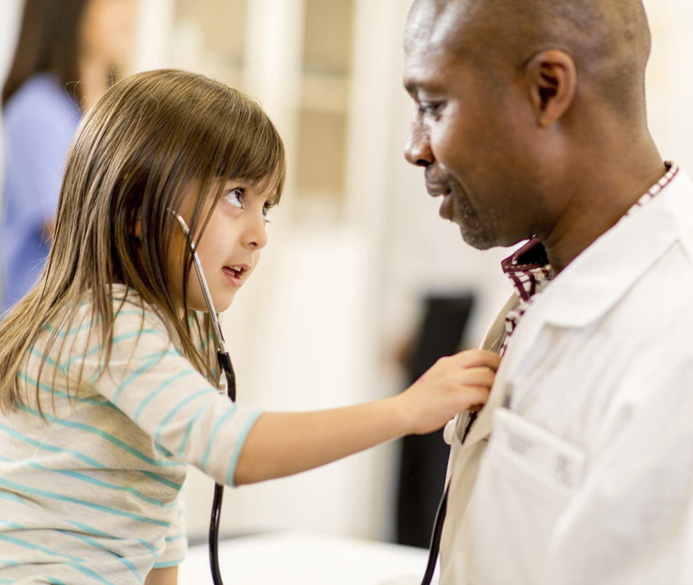 Small girl holding a stethoscope to a male doctor's chest