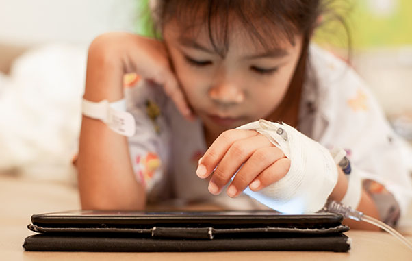 Young girl with bandaged hand playing on tablet
