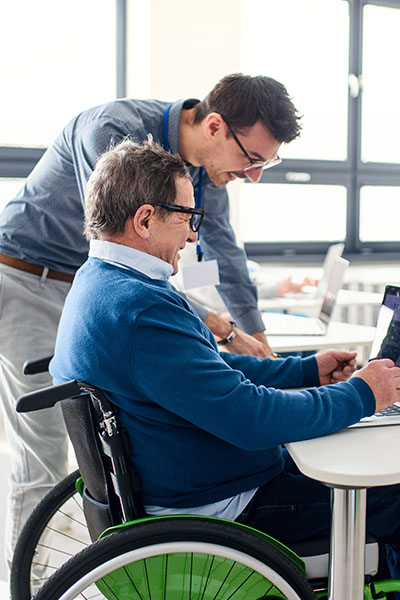 man in wheelchair looking at laptop with a carer